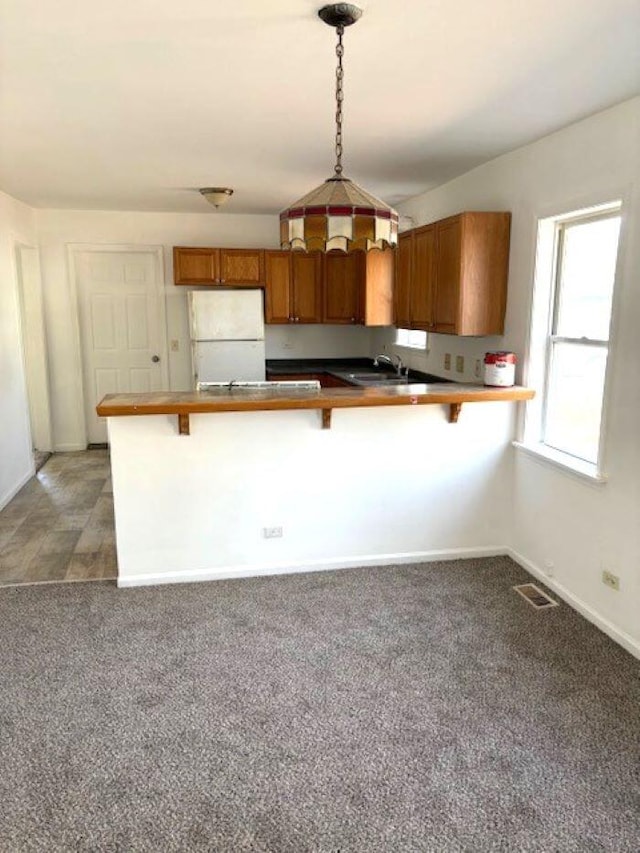 kitchen featuring brown cabinetry, visible vents, a breakfast bar, a peninsula, and freestanding refrigerator