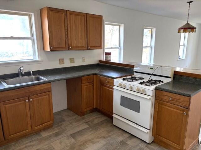 kitchen featuring brown cabinetry, a peninsula, gas range gas stove, a sink, and dark countertops