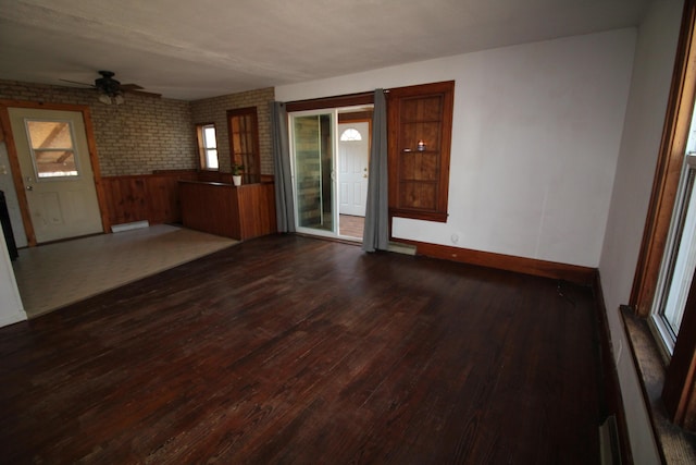 interior space with dark wood-style floors, brick wall, baseboards, and a ceiling fan