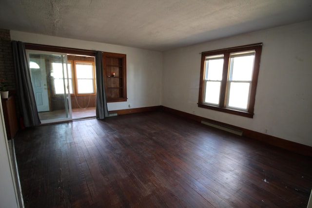 unfurnished room with dark wood finished floors, baseboards, a baseboard heating unit, and a wealth of natural light