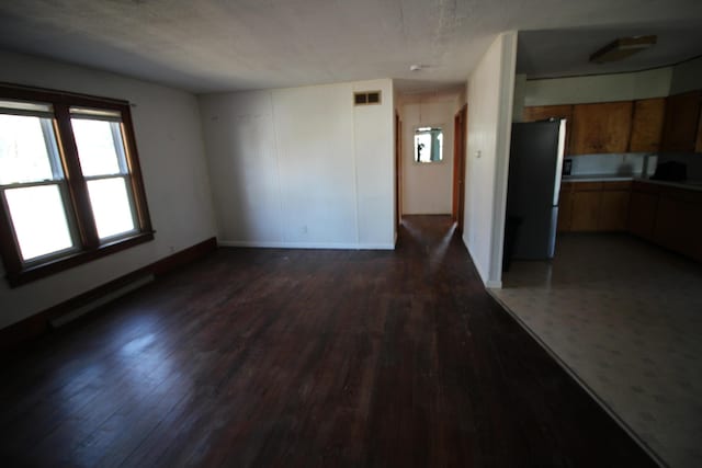 interior space featuring a baseboard heating unit, dark wood-type flooring, baseboards, and visible vents