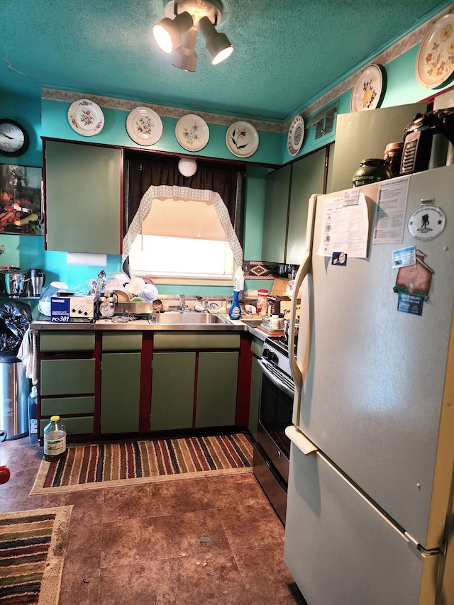 kitchen with stainless steel gas range oven, a sink, a textured ceiling, freestanding refrigerator, and green cabinets