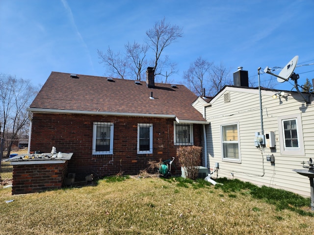 back of house with a lawn, brick siding, roof with shingles, and a chimney