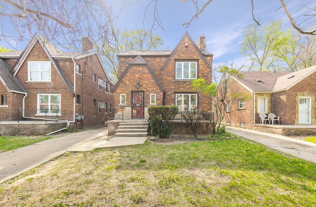 tudor home featuring a chimney, a front lawn, and brick siding