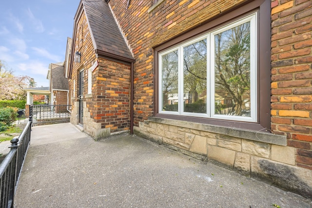 view of property exterior featuring brick siding, a shingled roof, and a patio area