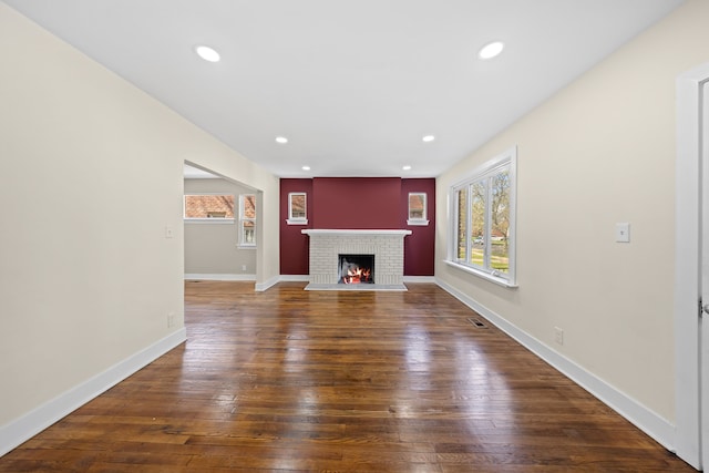 unfurnished living room featuring baseboards, wood-type flooring, a brick fireplace, and recessed lighting