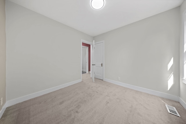 spare room featuring baseboards, visible vents, and light carpet