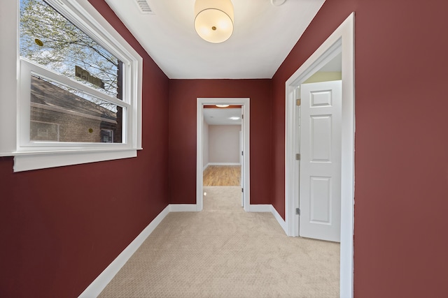 hall with baseboards, light colored carpet, and visible vents