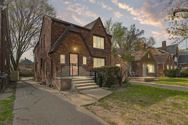 tudor-style house featuring fence, a lawn, and brick siding
