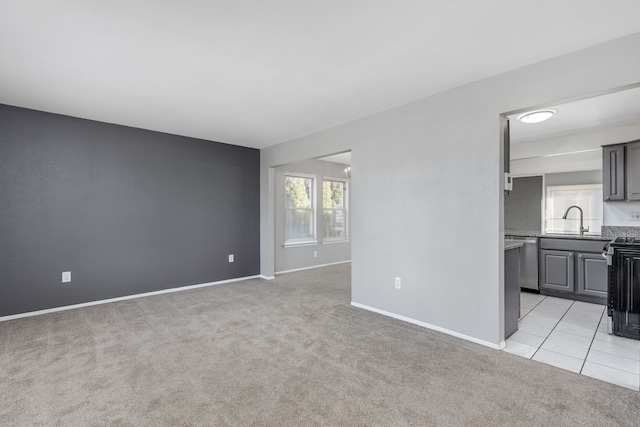 unfurnished living room featuring light tile patterned flooring, light colored carpet, baseboards, and a sink