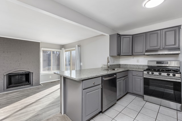 kitchen featuring a peninsula, a sink, gray cabinetry, under cabinet range hood, and appliances with stainless steel finishes