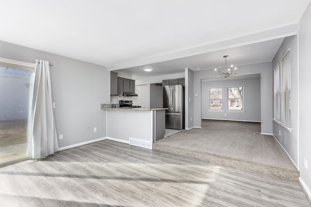 unfurnished living room with light wood-type flooring, visible vents, baseboards, and a notable chandelier