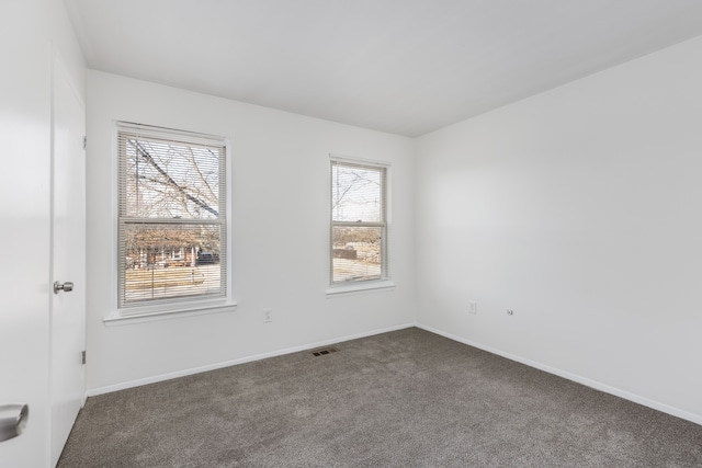 empty room featuring visible vents, baseboards, and dark carpet