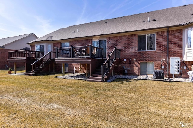 rear view of house with brick siding, stairway, a wooden deck, roof with shingles, and a lawn