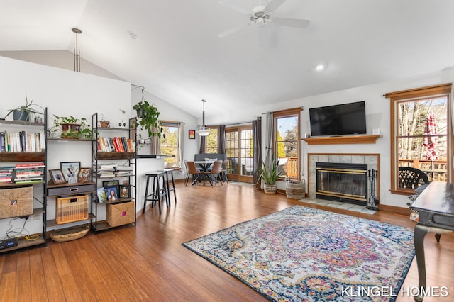 living area featuring wood finished floors, ceiling fan, a tile fireplace, and vaulted ceiling