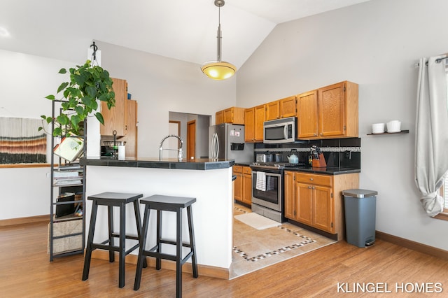 kitchen featuring dark countertops, decorative backsplash, appliances with stainless steel finishes, a kitchen breakfast bar, and a sink