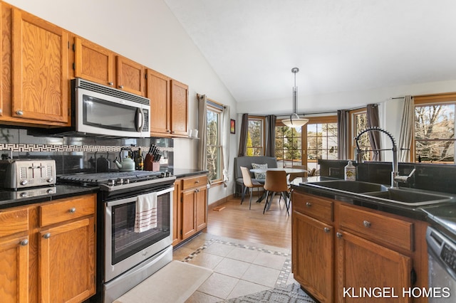 kitchen with a sink, dark countertops, appliances with stainless steel finishes, and vaulted ceiling