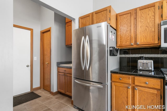 kitchen with light tile patterned floors, brown cabinets, tasteful backsplash, and freestanding refrigerator