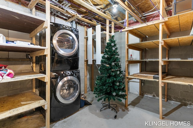 laundry room featuring concrete block wall, laundry area, and stacked washer / dryer