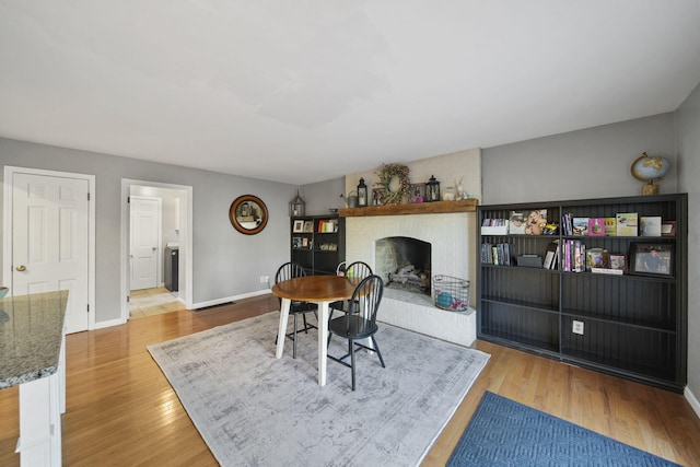 dining area with baseboards, a brick fireplace, and wood finished floors