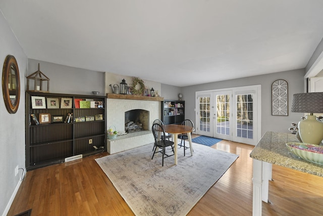 dining space with wood finished floors, visible vents, baseboards, a fireplace, and french doors