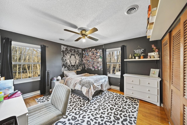 bedroom with visible vents, a textured ceiling, wood finished floors, and a ceiling fan