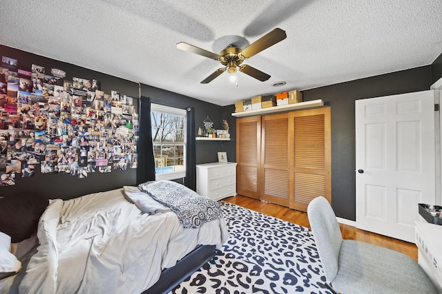 bedroom with a closet, a textured ceiling, light wood-style floors, and a ceiling fan