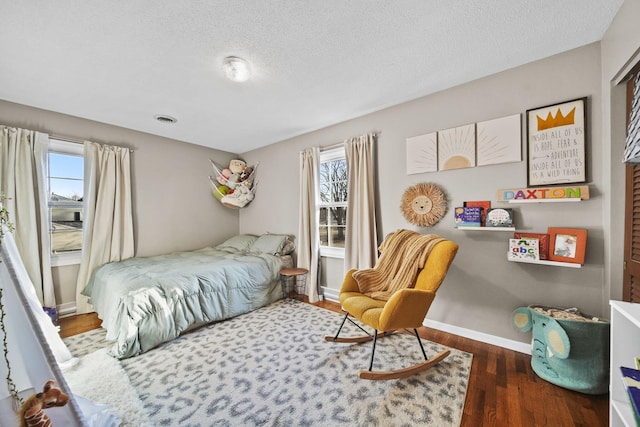 bedroom featuring a textured ceiling, wood finished floors, visible vents, and baseboards