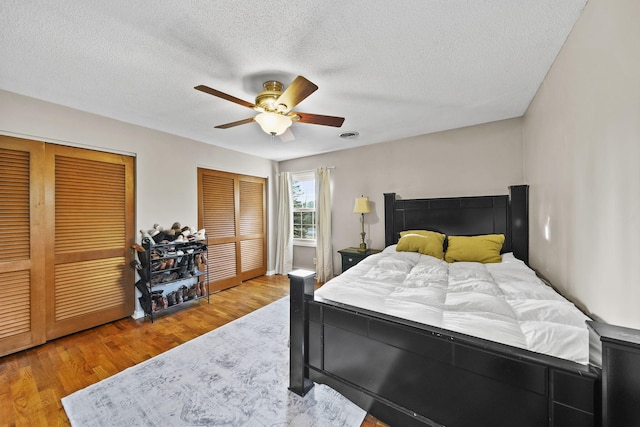 bedroom featuring a ceiling fan, wood finished floors, two closets, and a textured ceiling