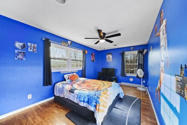 bedroom with a ceiling fan, wood finished floors, baseboards, and a textured ceiling