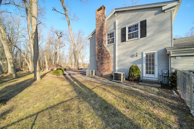 rear view of house featuring fence, entry steps, central AC unit, a lawn, and a chimney