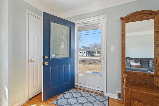 foyer entrance with baseboards, visible vents, light wood-type flooring, and ornamental molding