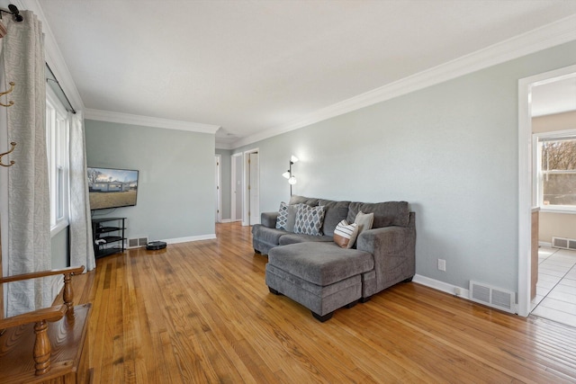 living room with visible vents, baseboards, light wood-style flooring, and crown molding