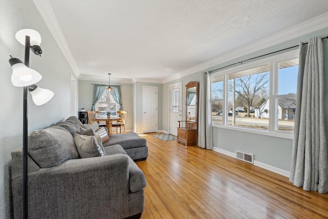 living room featuring baseboards, visible vents, light wood finished floors, a textured ceiling, and crown molding