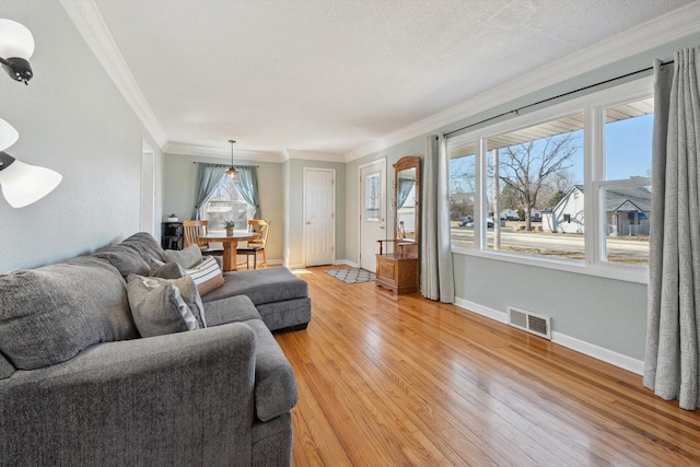 living area with ornamental molding, visible vents, a wealth of natural light, and light wood-type flooring