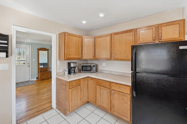 kitchen with stainless steel microwave, freestanding refrigerator, recessed lighting, light countertops, and light tile patterned floors