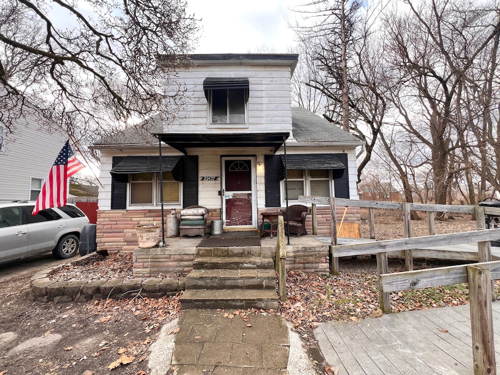 bungalow featuring stone siding, roof with shingles, and covered porch