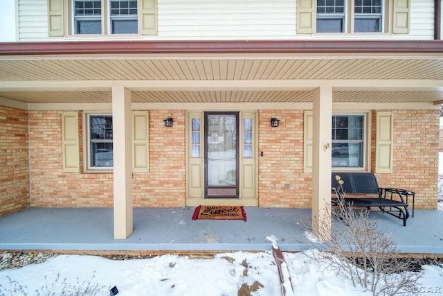 snow covered property entrance featuring brick siding and a porch