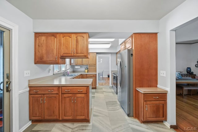 kitchen featuring a sink, brown cabinetry, light countertops, and freestanding refrigerator