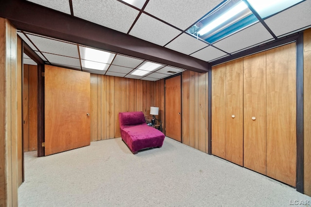 living area featuring wooden walls, carpet, and a drop ceiling