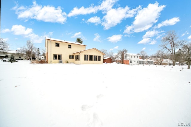 snow covered back of property featuring a sunroom