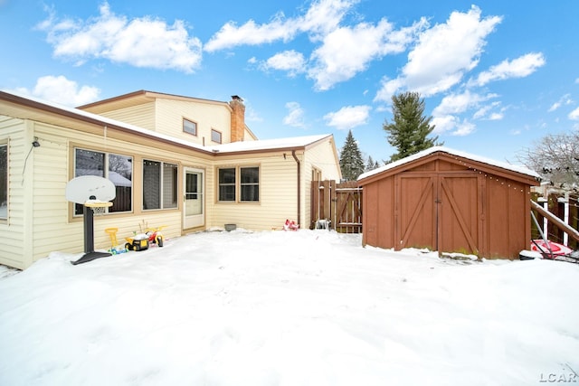 snow covered back of property with an outbuilding, a shed, a chimney, and fence