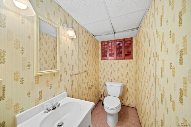 half bath featuring wallpapered walls, vanity, toilet, and a paneled ceiling