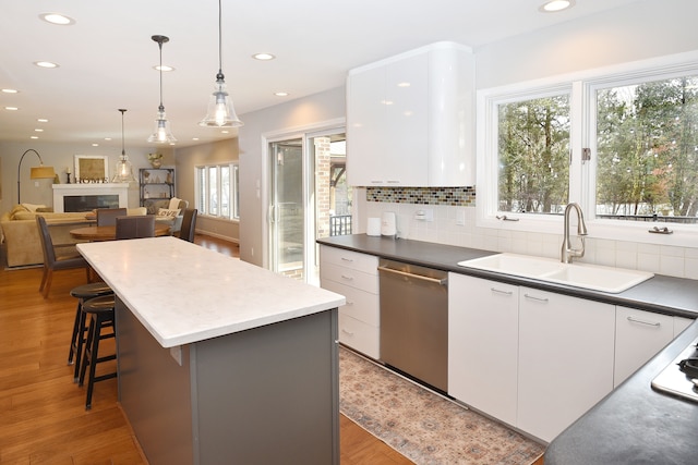 kitchen with light wood finished floors, a kitchen island, a sink, stainless steel dishwasher, and backsplash