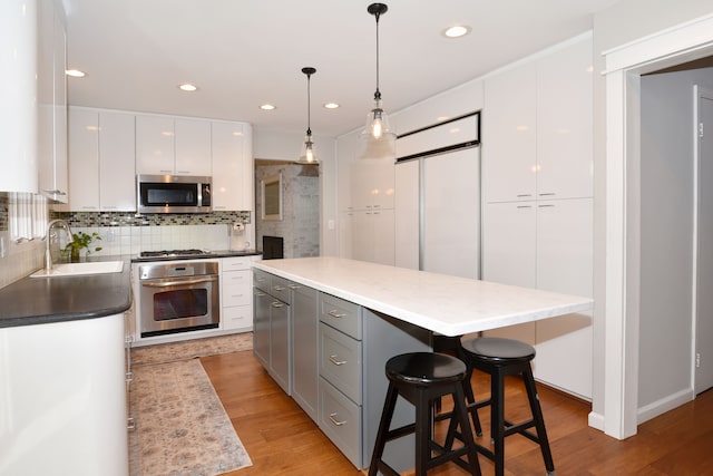 kitchen with tasteful backsplash, light wood-type flooring, appliances with stainless steel finishes, white cabinets, and a sink