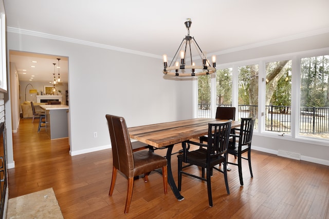 dining room featuring wood finished floors, visible vents, baseboards, crown molding, and a notable chandelier