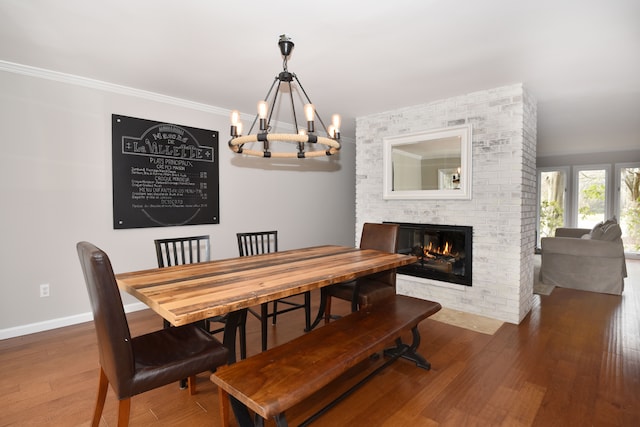 dining area with a brick fireplace, ornamental molding, wood finished floors, and a chandelier