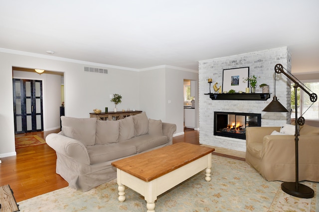 living room with wood finished floors, baseboards, visible vents, ornamental molding, and a brick fireplace