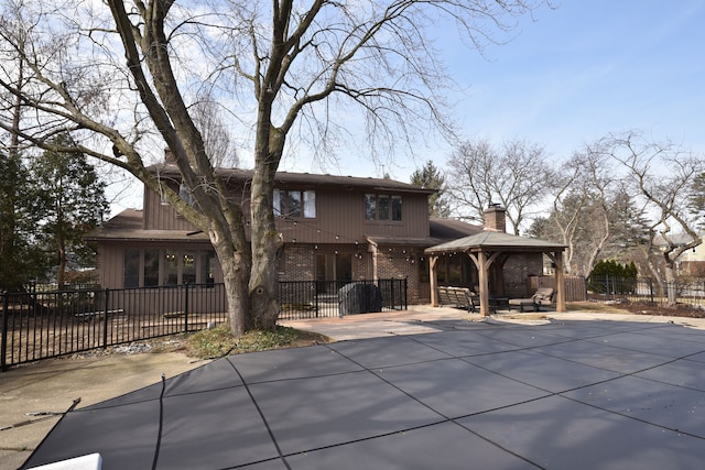 rear view of property featuring brick siding, fence, a gazebo, a chimney, and a patio area