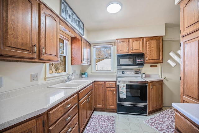 kitchen with a sink, range with electric stovetop, brown cabinetry, black microwave, and light countertops